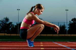 imagen de hermosa joven europeo hembra corredor o sprinter sentado en al aire libre estadio pista, sensación agotado después pique o maratón. foto