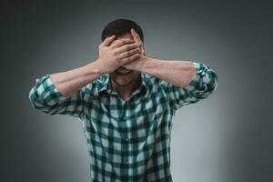 Man covering his eyes with hand, casual clothing. Studio shot. photo