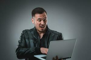 Man in black jacket looking at laptop, half turn. Holding opened laptop and working. Emotion. photo