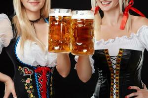 Young and beautiful bavarian girls with two beer mugs on black background photo