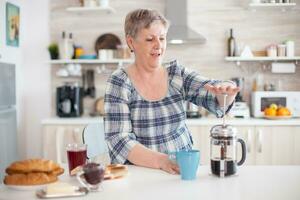 Mature woman using french press to make coffee in kitchen during breakfast. Elderly person in the morning enjoying fresh brown cafe espresso cup caffeine from vintage mug, filter relax refreshment photo