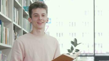 alegre jovem homem sorridente enquanto lendo uma livro às Faculdade biblioteca video