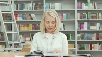 charmig ung kvinna leende till de kamera medan läsning på de bibliotek video