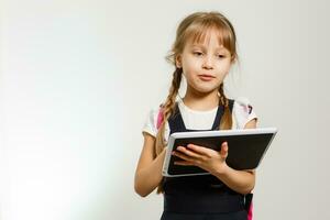 el pequeño niña utilizando el tableta en el blanco pared antecedentes foto