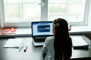 Little girl studying online using her laptop at home photo