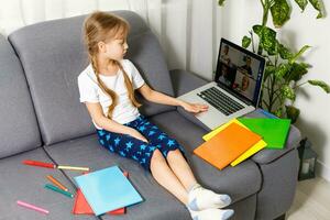 The girl at home communicates with friends on the Internet. Kids distance learning. Cute little girl using laptop at home. Education, online study, home studying, schoolgirl children lifestyle concept photo