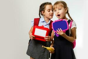 Pupils of primary school with lunch-boxes in hands. Girls with backpacks are eating fruit. Beginning of lessons. First day of fall. photo