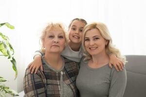 Three generations of women. Beautiful woman and teenage girl are kissing their granny while sitting on couch at home photo