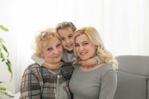 Portrait of three generations of women look at camera posing for family picture, cute little girl hug mom and granny enjoy time at home, smiling mother, daughter and grandmother spend weekend together photo