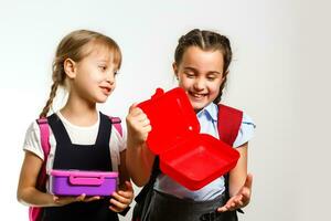 Pupils of primary school with lunch-boxes in hands. Girls with backpacks are eating fruit. Beginning of lessons. First day of fall. photo