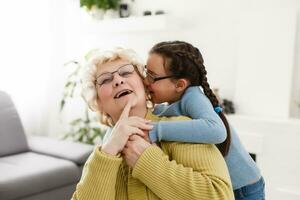 Senior woman hugging granddaughter while sitting on sofa at home photo