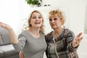 Self portrait of pretty charming positive funky mother and daughter shooting selfie on front camera having video-call sitting in modern white living room enjoying meeting free time photo