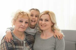 Portrait of three generations of women look at camera posing for family picture, cute little girl hug mom and granny enjoy time at home, smiling mother, daughter and grandmother spend weekend together photo