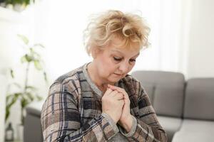 Religious faithful middle aged woman praying with hope faith holding hands clasped together in namaste at home in morning, old mature lady believer christian saying worship prayer photo