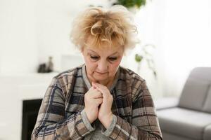 Religious faithful middle aged woman praying with hope faith holding hands clasped together in namaste at home in morning, old mature lady believer christian saying worship prayer photo