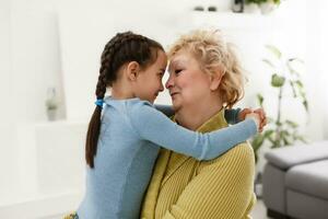 Senior woman hugging granddaughter while sitting on sofa at home photo