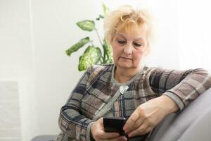 Concept of easy, fast usage of modern technology among all ages. Portrait of confident mature woman with wrinkles she is using her modern smartphone for sending a message isolated on gray background photo