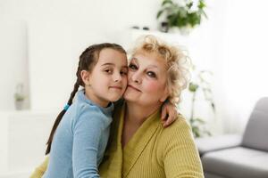 Senior woman hugging granddaughter while sitting on sofa at home photo