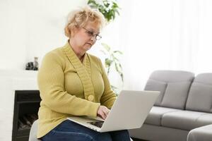 Old woman working on laptop computer at home, Grandma using notebook and searching on internet site photo