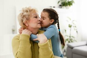 Senior woman hugging granddaughter while sitting on sofa at home photo