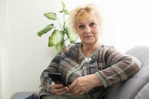 Concept of easy, fast usage of modern technology among all ages. Portrait of confident mature woman with wrinkles she is using her modern smartphone for sending a message isolated on gray background photo