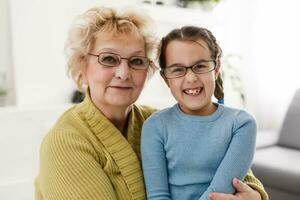 Portrait of happy old grandmother and kid girl looking at camera, smiling grandma with granddaughter making video call, child and granny vloggers recording video blog or vlog together photo