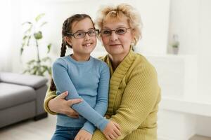 Portrait of happy old grandmother and kid girl looking at camera, smiling grandma with granddaughter making video call, child and granny vloggers recording video blog or vlog together photo