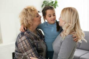 Three generations of women. Beautiful woman and teenage girl are kissing their granny while sitting on couch at home photo