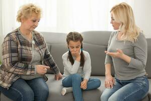 Little girl sitting at home crying while mom and granny scolding her photo