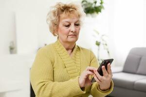 Concept of easy, fast usage of modern technology among all ages. Portrait of confident mature woman with wrinkles she is using her modern smartphone for sending a message isolated on gray background photo