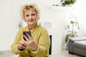 Concept of easy, fast usage of modern technology among all ages. Portrait of confident mature woman with wrinkles she is using her modern smartphone for sending a message isolated on gray background photo