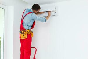 Young Man Repairing Air Conditioner Standing On Stepladder photo