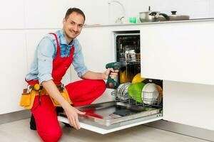 masculino técnico sentado cerca lavavajillas en cocina foto