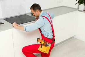 Young Man In Overall Installing Induction Stove photo