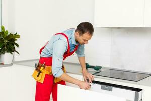 Handyman fixing kitchen's cabinet with screwdriver photo