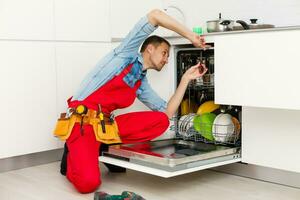 Male Technician Sitting Near Dishwasher In Kitchen photo