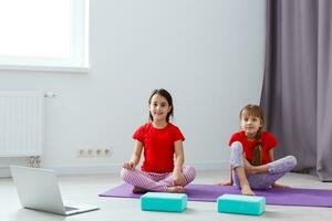 dos niñas practicando yoga, estiramientos, fitness por video en el cuaderno. entrenamiento de educación en línea distante, aeróbico en casa. estilo de vida saludable, coronavirus, quédate en casa. los niños hacen deporte en casa en cuarentena. foto