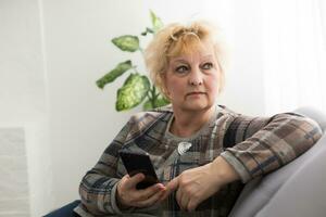 Concept of easy, fast usage of modern technology among all ages. Portrait of confident mature woman with wrinkles she is using her modern smartphone for sending a message isolated on gray background photo