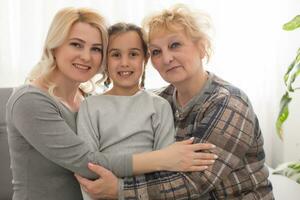 Three generations of women. Beautiful woman and teenage girl are kissing their granny while sitting on couch at home photo