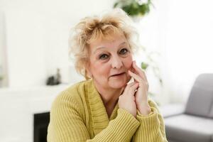 Attractive elderly woman sitting on couch at home, looking at camera, makes video call, communication distantly, modern wireless technologies concept photo