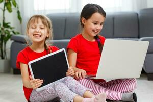 dos pequeño muchachas sentado en frente de un ordenador portátil y reír, de cerca, positivo emociones, entretenimiento en el Internet para niños foto