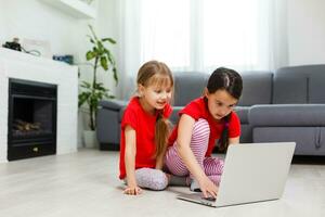 dos pequeño muchachas son jugando con ordenador portátil en cuarto de jugar a hogar foto