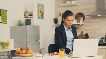 Business woman eating toasted bread with butter while working on laptop during breakfast. Concentrated business woman in the morning multitasking in the kitchen before going to the office, stressful way of life, career and goals to meet photo