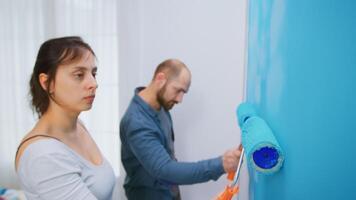 Woman painting wall with roller brush while redecorating apartment living room. Couple redecorating together. Apartment redecoration and home construction while renovating and improving. Repair and decorating. photo