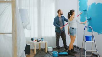 Couple painting wall using roller paint brush. Painting wall with blue paint. Color change. Renovate, renovation, construction. Apartment redecoration and home construction while renovating and improving. Repair and decorating. photo