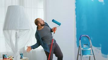 Happy repairman singing on roller brush during home renovation. Painting with blue paint. Apartment redecoration and home construction while renovating and improving. Repair and decorating. photo