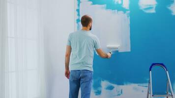 Covering wall blue paint with white paint using roller brush. Handyman renovating. Apartment redecoration and home construction while renovating and improving. Repair and decorating. photo