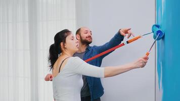 Couple repainting apartment wall with blue paint using roller brush. Apartment redecoration and home construction while renovating and improving. Repair and decorating. photo