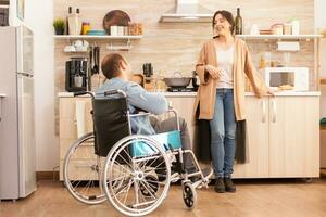 Disabled man sitting in chair and talking with wife while preparing meal. Disabled paralyzed handicapped man with walking disability integrating after an accident. photo