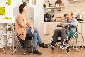 Disabled man in wheelchair and wife smiling at each other in kitchen. Disabled paralyzed handicapped man with walking disability integrating after an accident. photo